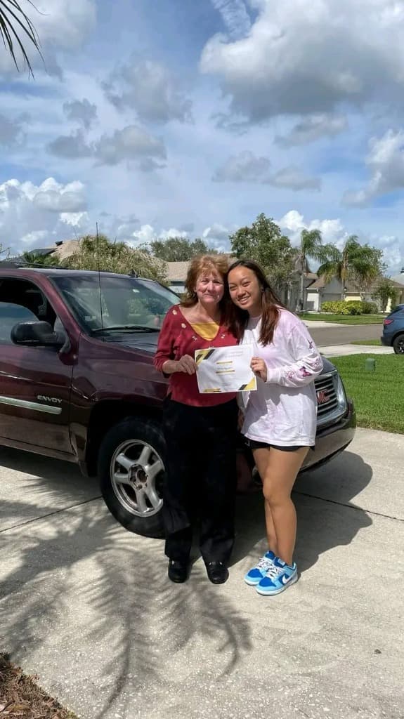 Student with instructor holding certificate by a Class E Driving car